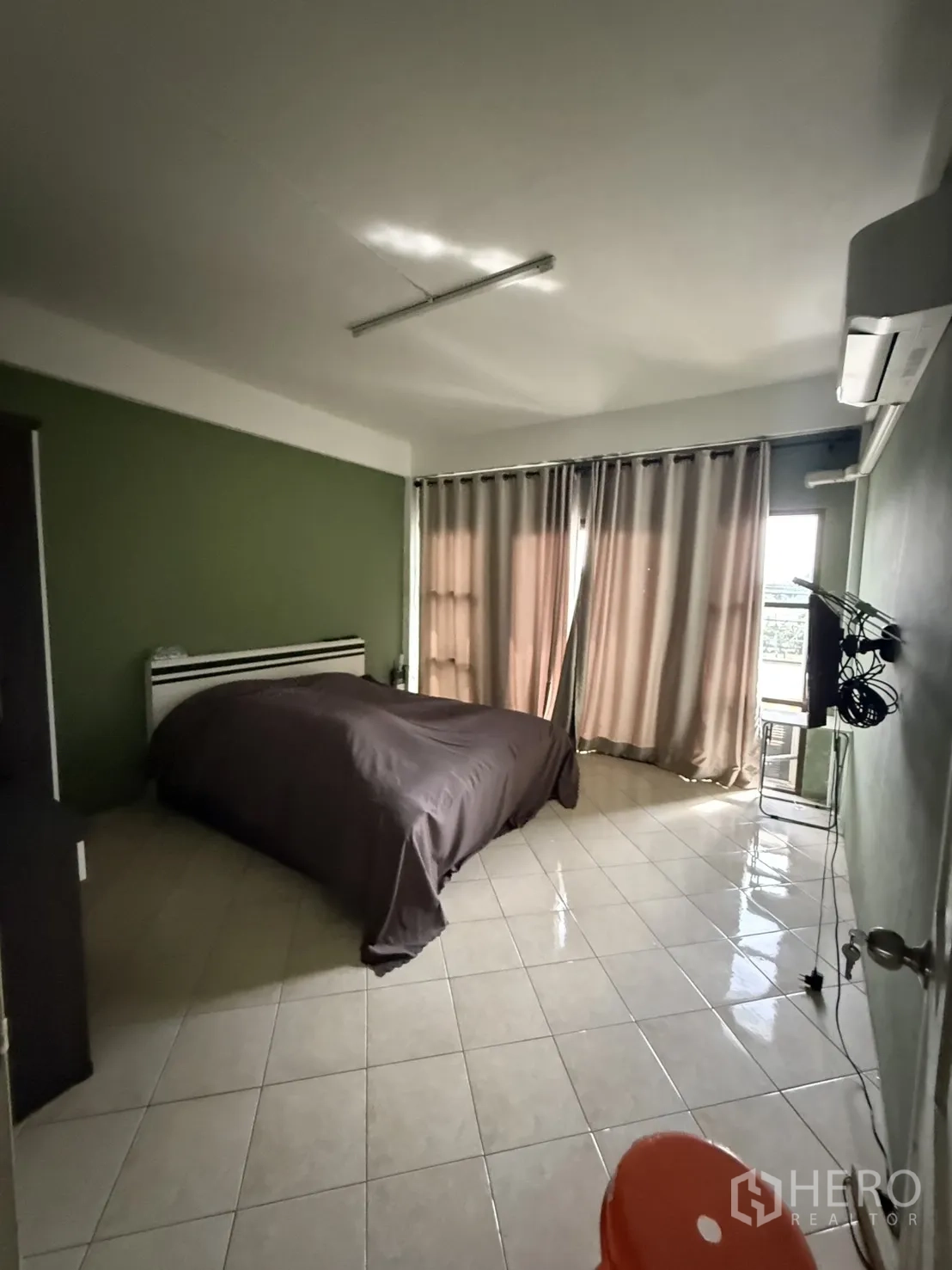 Shophouse for rent in Pak Kret, Nonthaburi - Upper-floor bedroom with double bed, tile floor, air conditioner, and curtains.