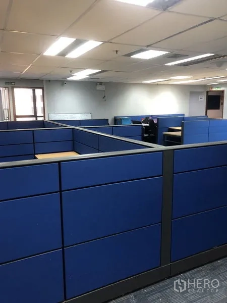 Office Space for rent - Open-plan workspace with blue partitioned cubicles under fluorescent ceiling lights.
