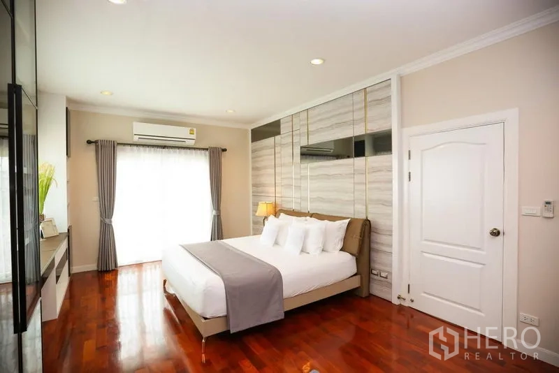 บ้าน ให้เช่าในBang Na, Bangkok - ห้องนอนมาสเตอร์ พื้นไม้ เตียงคิง ผนังตกแต่ง และผ้าม่านบานประตูระเบียง