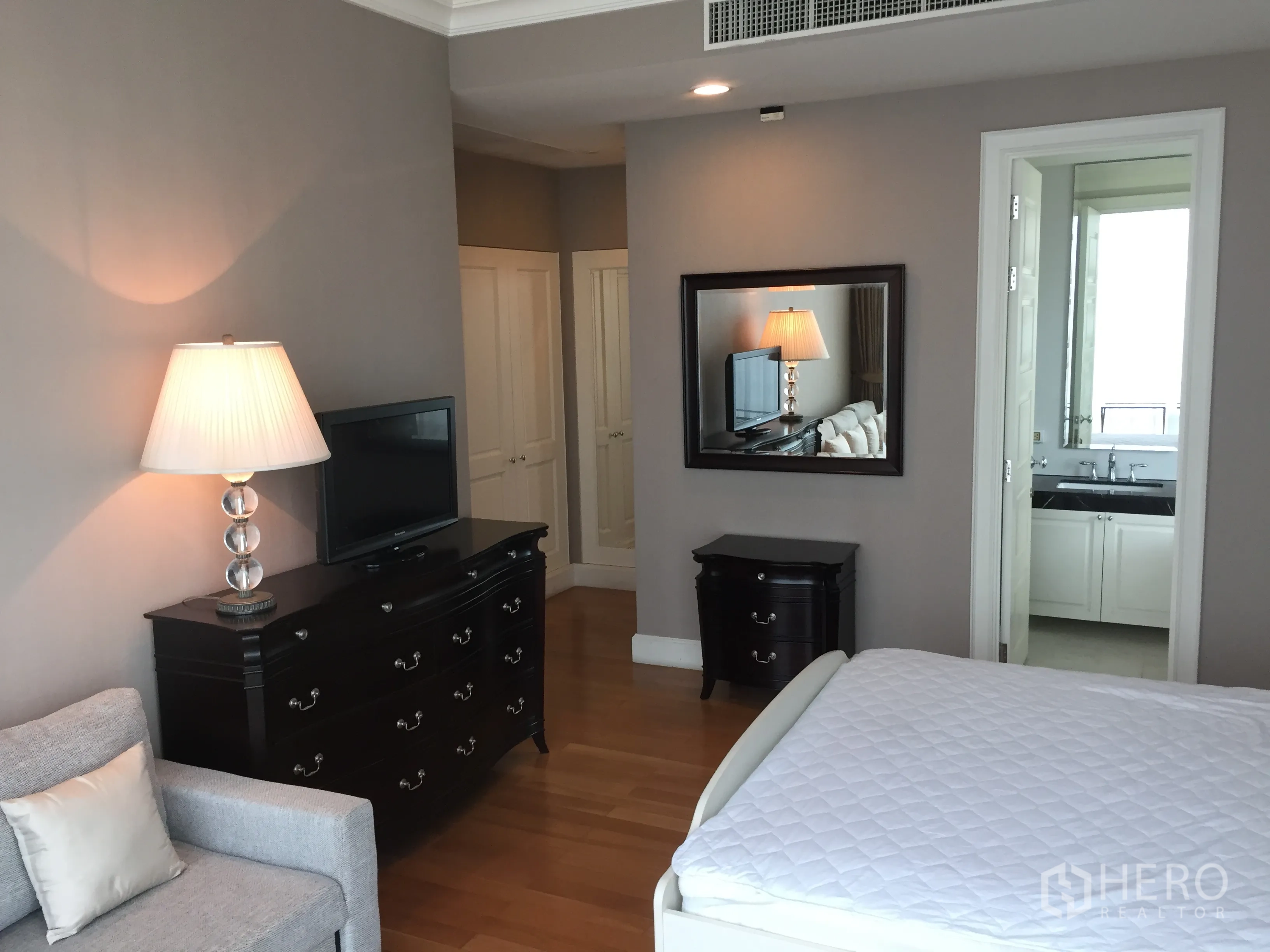 Condominium for rent in Watthana, Bangkok - Master bedroom with hardwood floors, dark wood dresser and ensuite bathroom entrance.