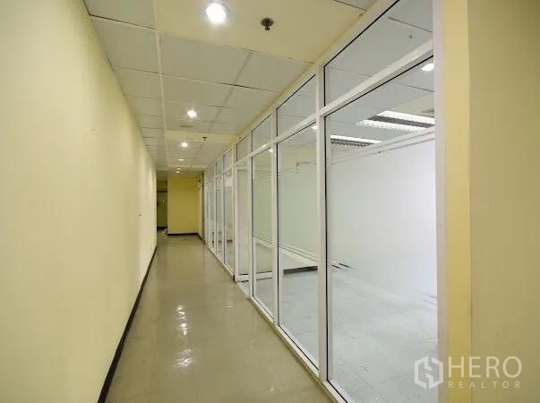 办公空间 出租在Watthana, Bangkok - 长走廊与玻璃幕墙办公室并行，嵌入式照明和抛光地砖。