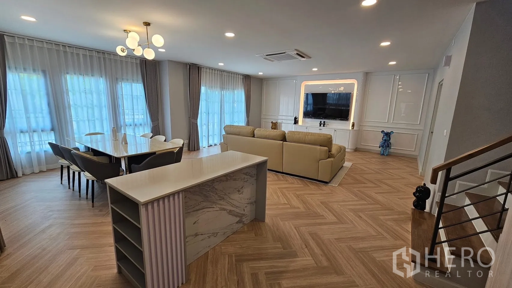 独立式住宅 出租或出售在Bang Phli, Samut Prakan - 采光充足的客餐一体空间，落地窗与纱帘，人字拼木地板，沙发与电视墙及岛台。