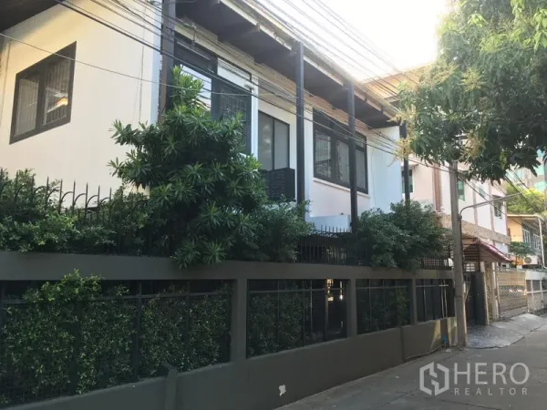 Detached House for rent in Watthana, Bangkok - Street-side façade of a two-storey detached house with privacy fence and mature greenery in Watthana.