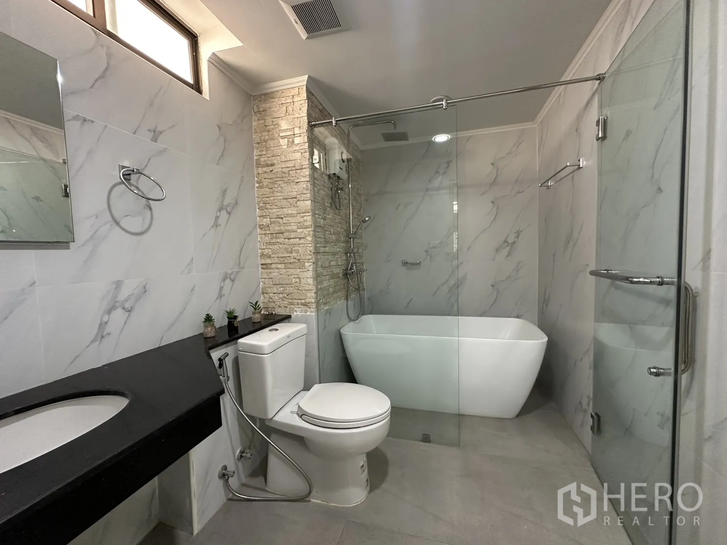 Condominium for rent in Watthana, Bangkok - Modern bathroom with freestanding tub, glass shower, and marble-effect tiles.