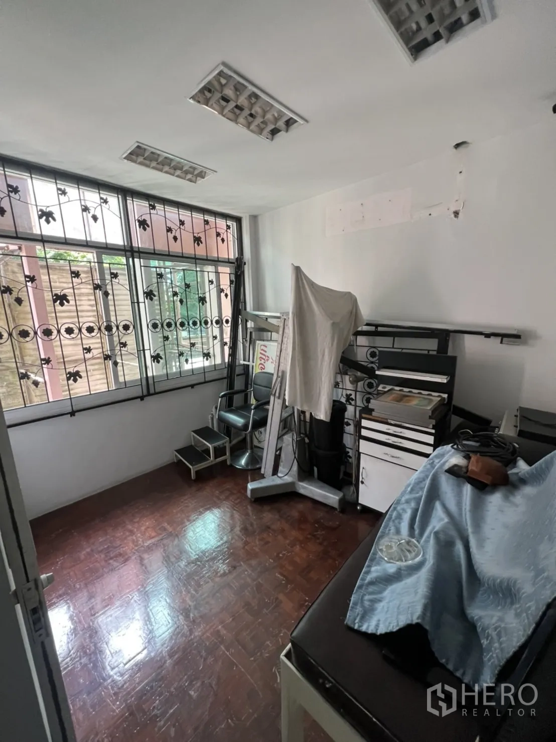 Shophouse for rent in Khlong Toei, Bangkok - Compact room with parquet flooring, barred windows and fluorescent light fixtures.