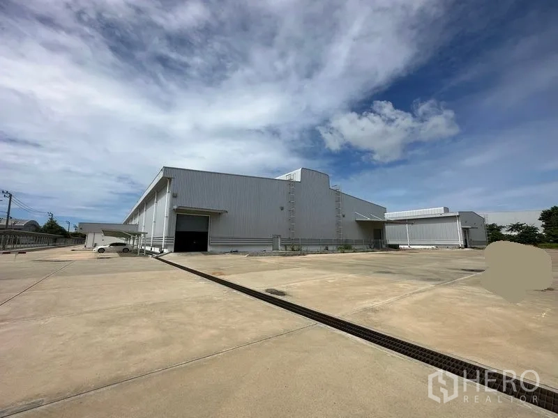 Factory for rent in Bang Sao Thong, Samut Prakan - Modern steel-clad factory exterior with a wide concrete yard and loading bay under blue sky.