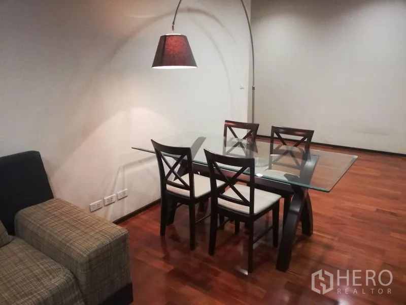 公寓 出租在Watthana, Bangkok - 餐区配玻璃餐桌四椅，拱形落地灯，旁边为沙发。