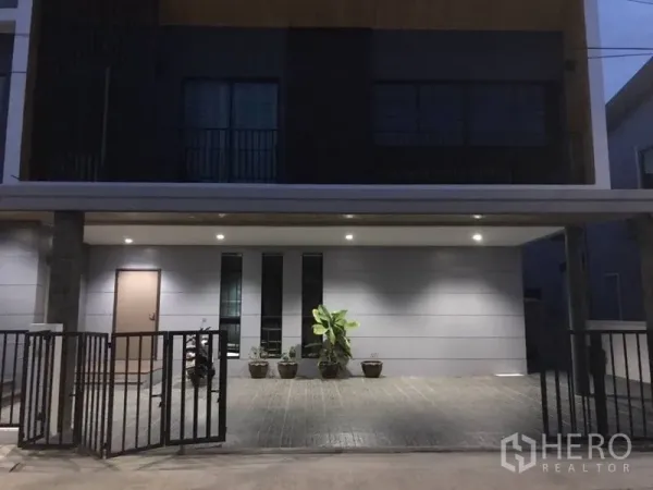 Detached House for rent in Thanyaburi, Pathum Thani - Contemporary house facade with gated driveway and under-roof parking lit by downlights.