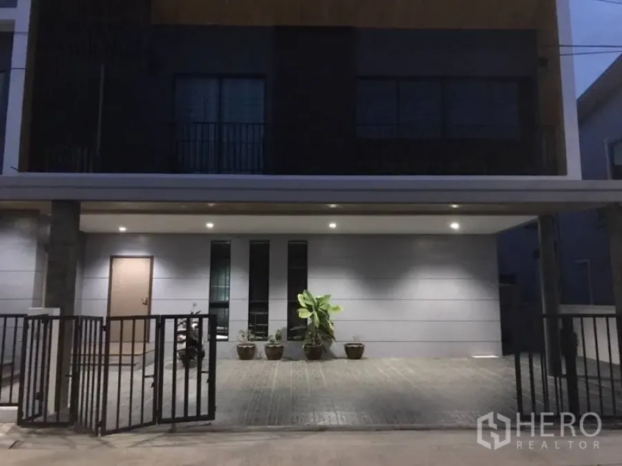 Detached House for rent in Thanyaburi, Pathum Thani - Contemporary house facade with gated driveway and under-roof parking lit by downlights.