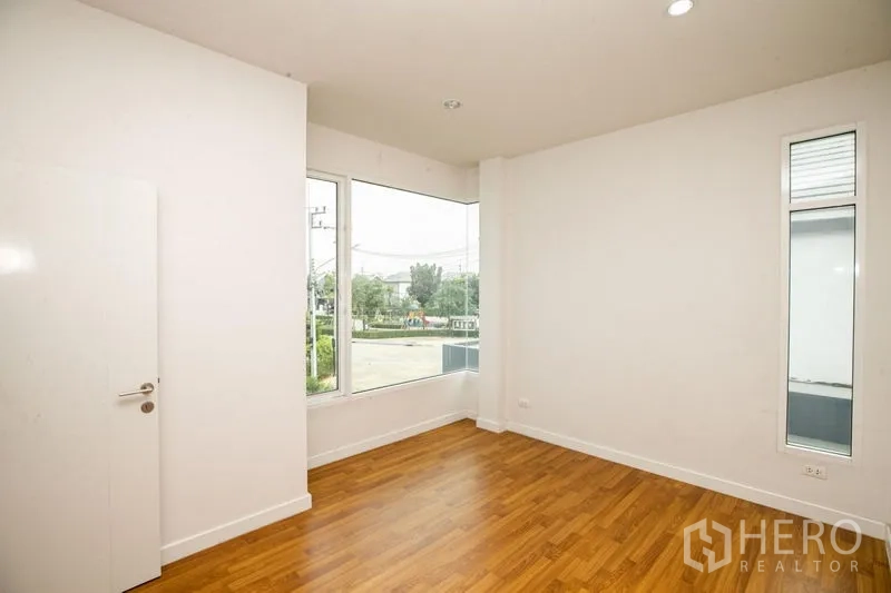 Detached House for rent or sale in Lam Luk Ka, Pathum Thani - Upper bedroom with a wide window facing neighboring modern homes.