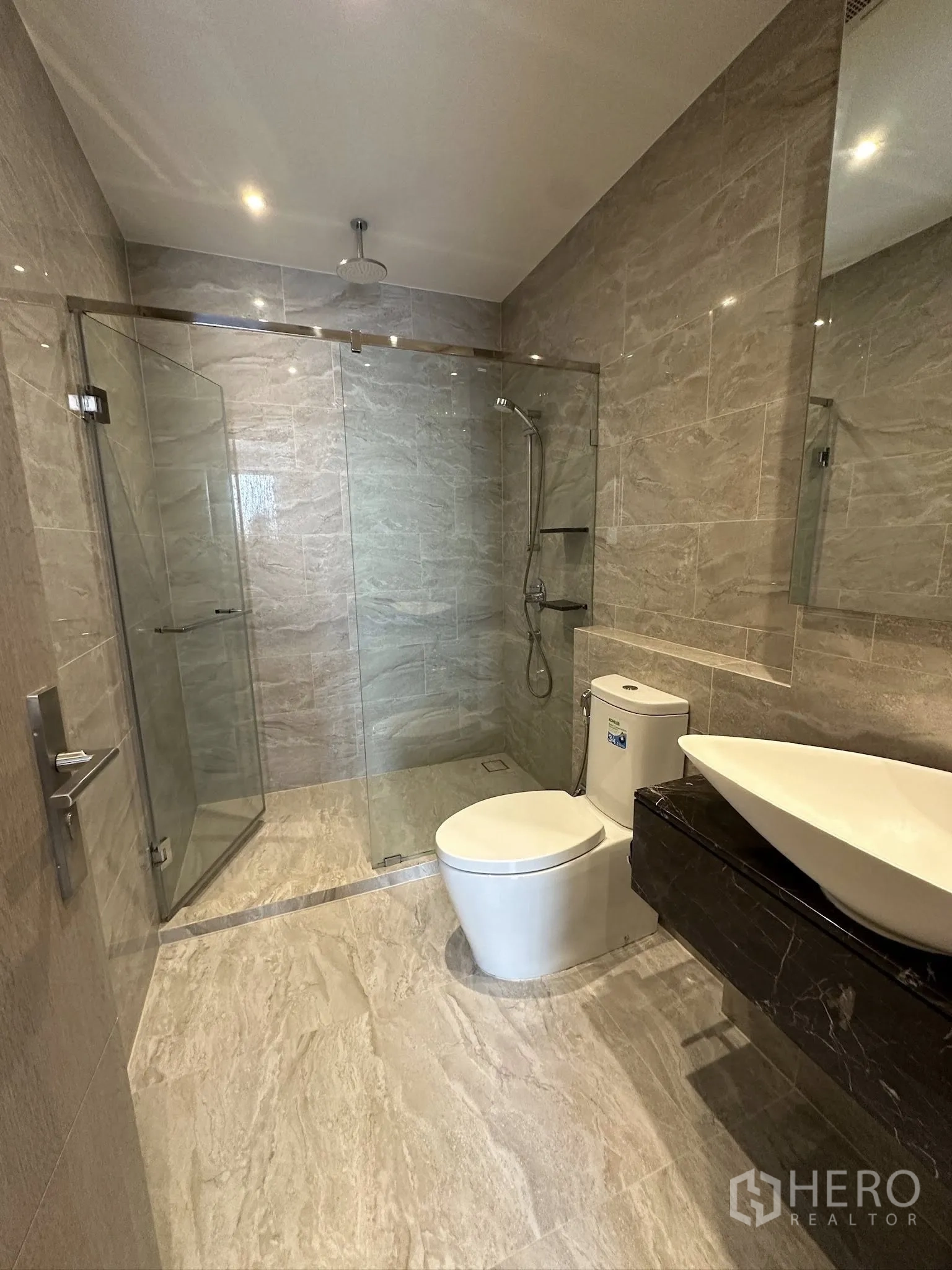 Condominium for sale in Din Daeng, Bangkok - Modern bathroom with glass-enclosed walk-in shower, rain showerhead, vessel sink, and stone-look tiles.