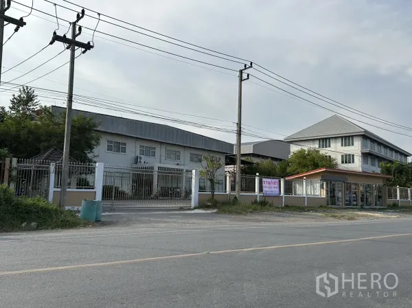 Factory for rent or sale in Lam Luk Ka, Pathum Thani - Angled exterior showing the factory gate, perimeter fence and guardhouse beside the main building.
