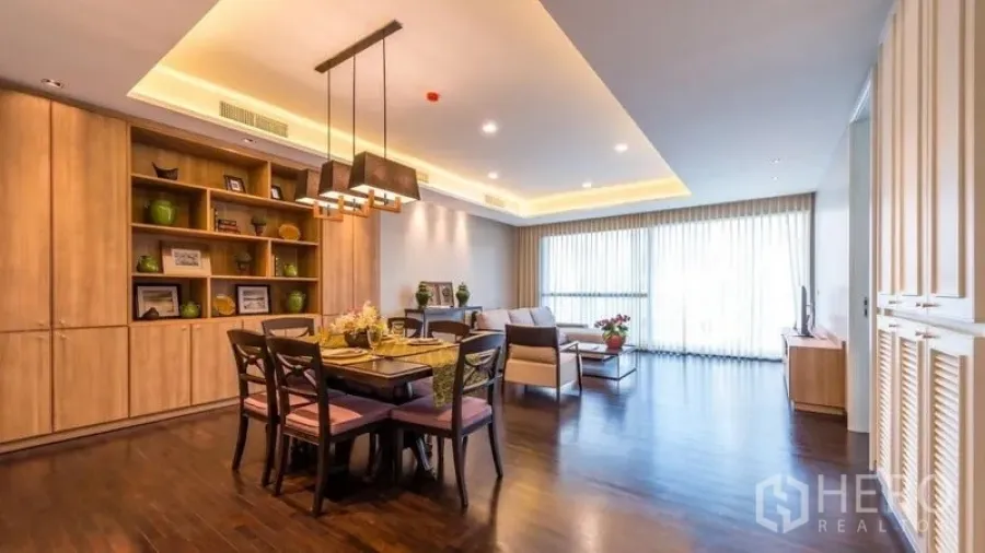 房间 出租在Pathum Wan, Bangkok - 开放式客餐厅，深色木地板，内置书柜，吊灯与落地窗帘采光充足。