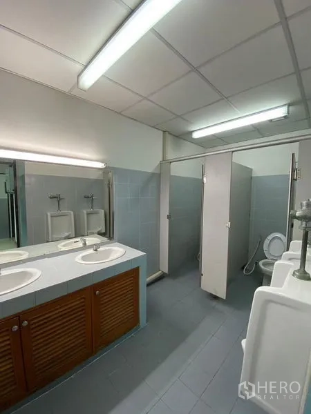 Office Space for rent - Well-maintained office restroom with dual sinks, urinals and toilet stalls under fluorescent lighting.