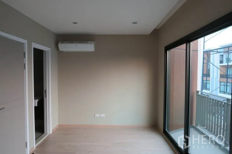 Townhouse for rent in Suan Luang, Bangkok - Bright bedroom with sliding door to a balcony, air-conditioning unit, and ensuite access.