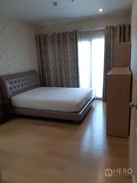 Condominium for rent in Phaya Thai, Bangkok - Bedroom with upholstered bed, wood flooring, blackout curtains, and balcony door letting in light.