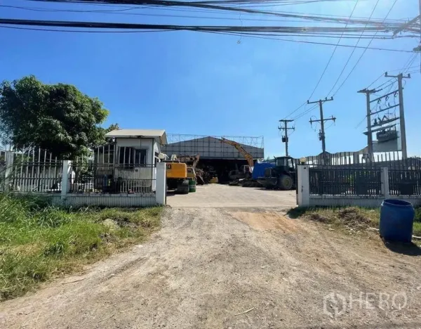 คลังสินค้า ให้เช่าในWang Noi, Phra Nakhon Si Ayutthaya - ทางเข้าโกดังพร้อมป้อมยาม ลานกว้าง ทางวิ่งสู่โรงเรือนโครงเหล็ก มีเครื่องจักรหนักและเสาไฟ ใต้ท้องฟ้าสีคราม.