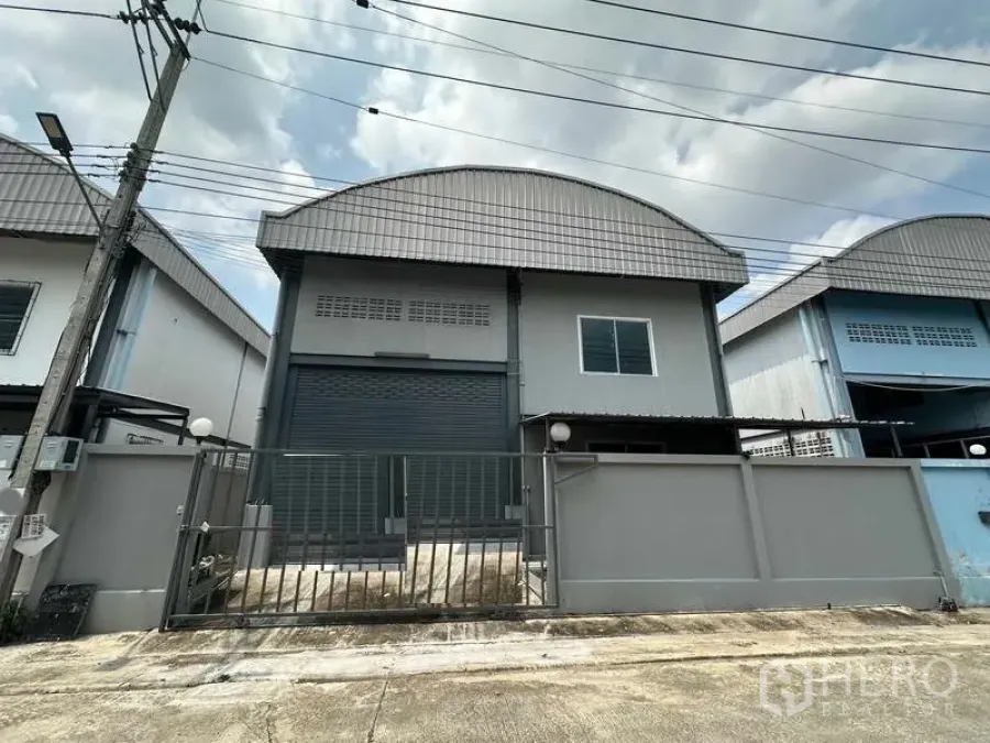 Warehouse for rent in Pak Kret, Nonthaburi - Gated modern warehouse facade with wide roller shutter and curved metal roof in Pak Kret.