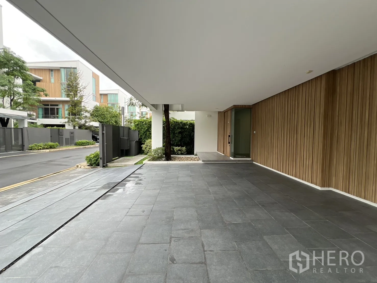 Detached House for rent in Saphan Sung, Bangkok - Covered driveway and entrance with grey tiles and vertical wood cladding.