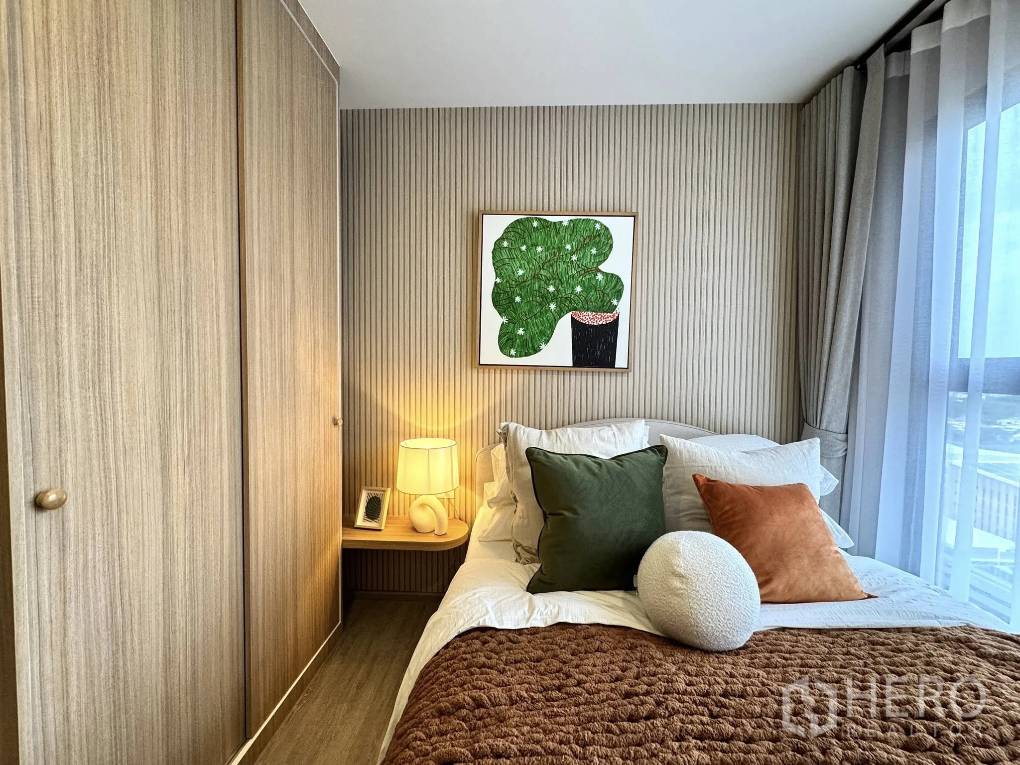 Condominium for rent in Watthana, Bangkok - Cozy bedroom with wood wardrobe, bedside lamp, wall art, and sheer-curtained window.