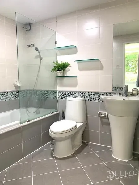 Condominium for rent or sale in Khlong Toei, Bangkok - Modern bathroom with bathtub, glass shower screen, pedestal sink, wall shelves and mosaic tile accent.
