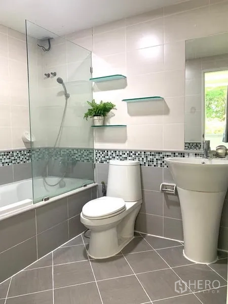 Condominium for rent or sale in Khlong Toei, Bangkok - Modern bathroom with bathtub, glass shower screen, pedestal sink, wall shelves and mosaic tile accent.