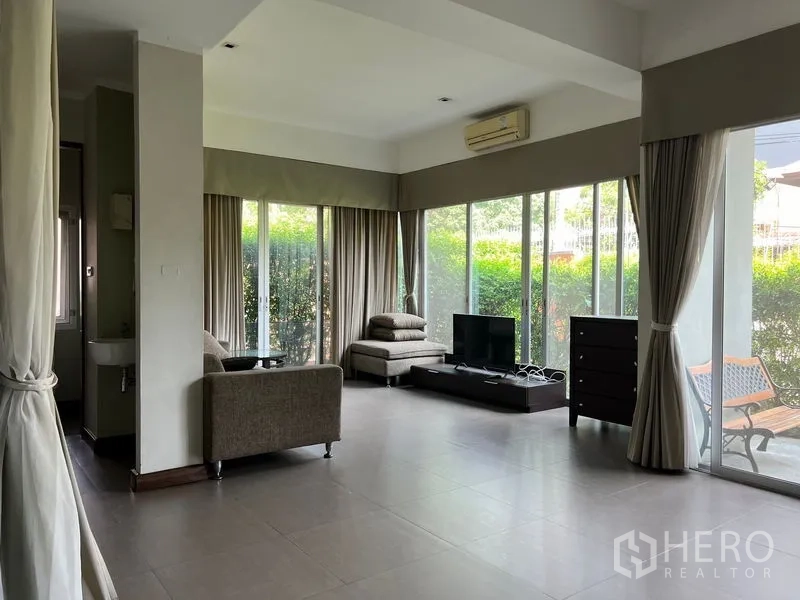 อพาร์ทเมนท์ ให้เช่าในWatthana, Bangkok - ห้องนั่งเล่นโปร่ง ผนังกระจกพื้นถึงเพดาน พื้นกระเบื้อง โซฟาและทีวี เปิดออกสู่เฉลียงและสวนพุ่ม