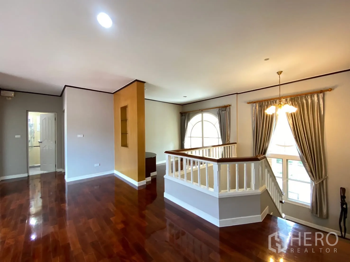 Detached House for rent in Phra Khanong, Bangkok - Upper landing living area with polished wood floors, white stair railing, large windows, and chandelier.
