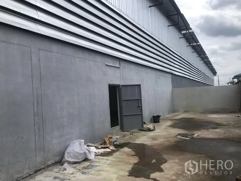 Factory for rent in Sai Noi, Nonthaburi - Rear service yard behind the factory with solid wall, side door and surface drainage.