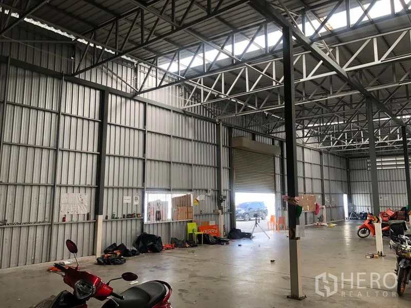 货栈 出租在Don Mueang, Bangkok - 高挑仓库墙面，带卷帘门与天窗采光带。