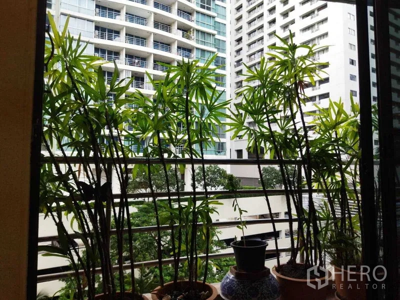 公寓 出租在Pathum Wan, Bangkok - 透过阳台绿植可见现代高楼与绿意庭院景观。