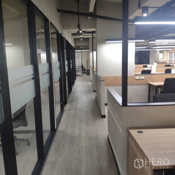 Office Space for rent - Walkway between glass offices and open-plan cubicles under linear LED lights.