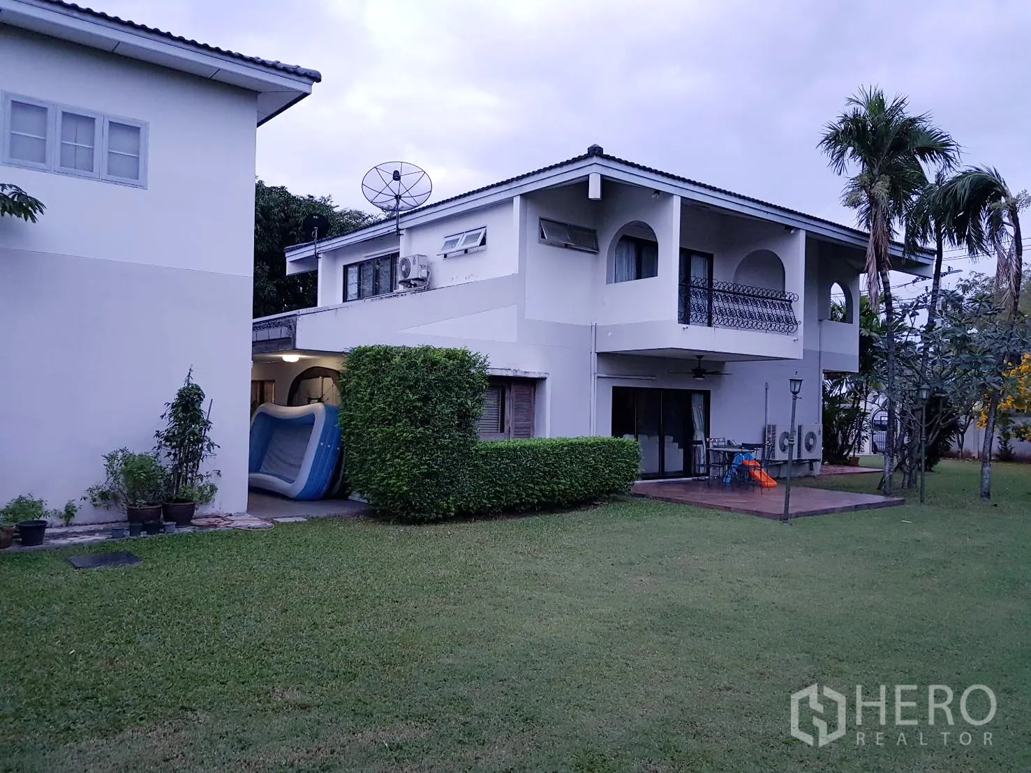 Detached House for rent in Khan Na Yao, Bangkok - Rear view of white two-storey house with balconies, wooden deck patio and wide green yard.