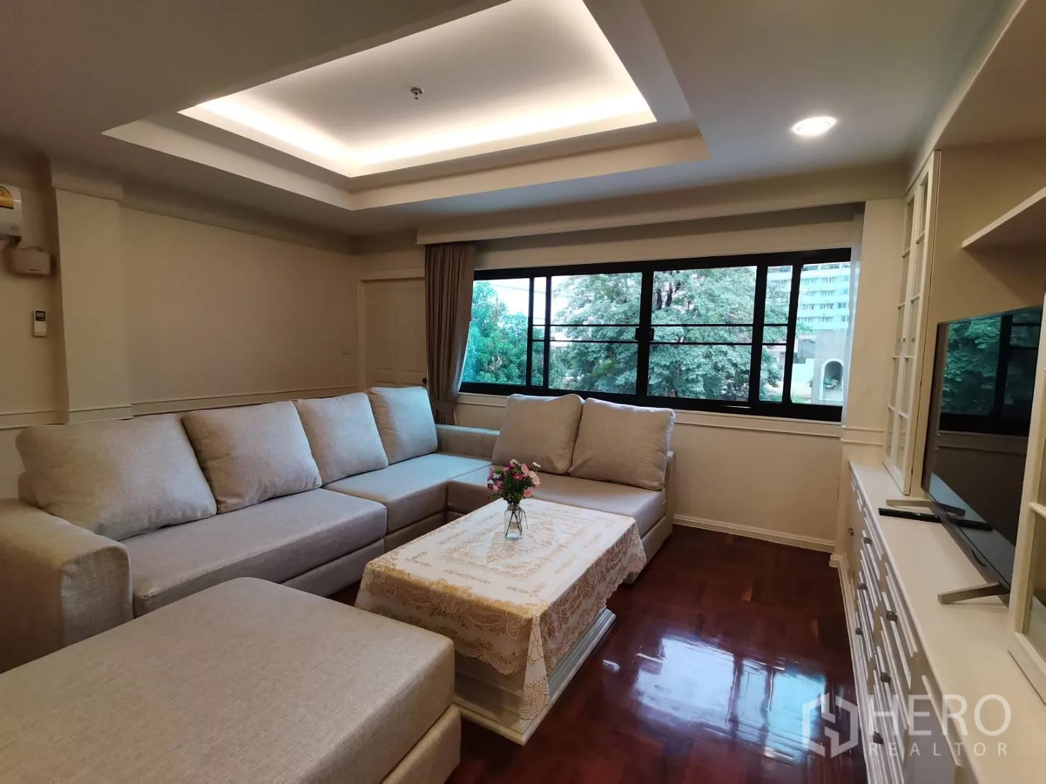 公寓 for rent in Watthana, Bangkok - 客厅设大窗、L形沙发、茶几与电视柜，景观郁郁葱葱。