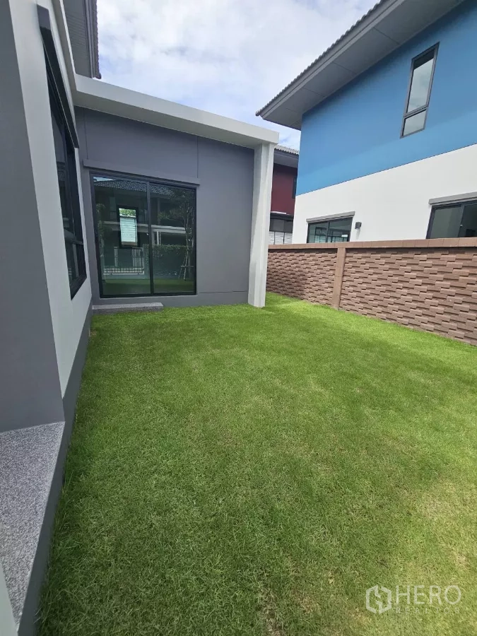 Detached House for sale in Lam Luk Ka, Pathum Thani - Side yard with green lawn beside the house and sliding door.