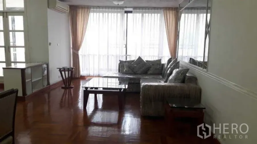 อพาร์ทเมนท์ ให้เช่าในPathum Wan, Bangkok - ห้องนั่งเล่นรับแสงธรรมชาติ โซฟาเข้ามุม โต๊ะกลาง กระจกผนัง และผ้าม่านสูง
