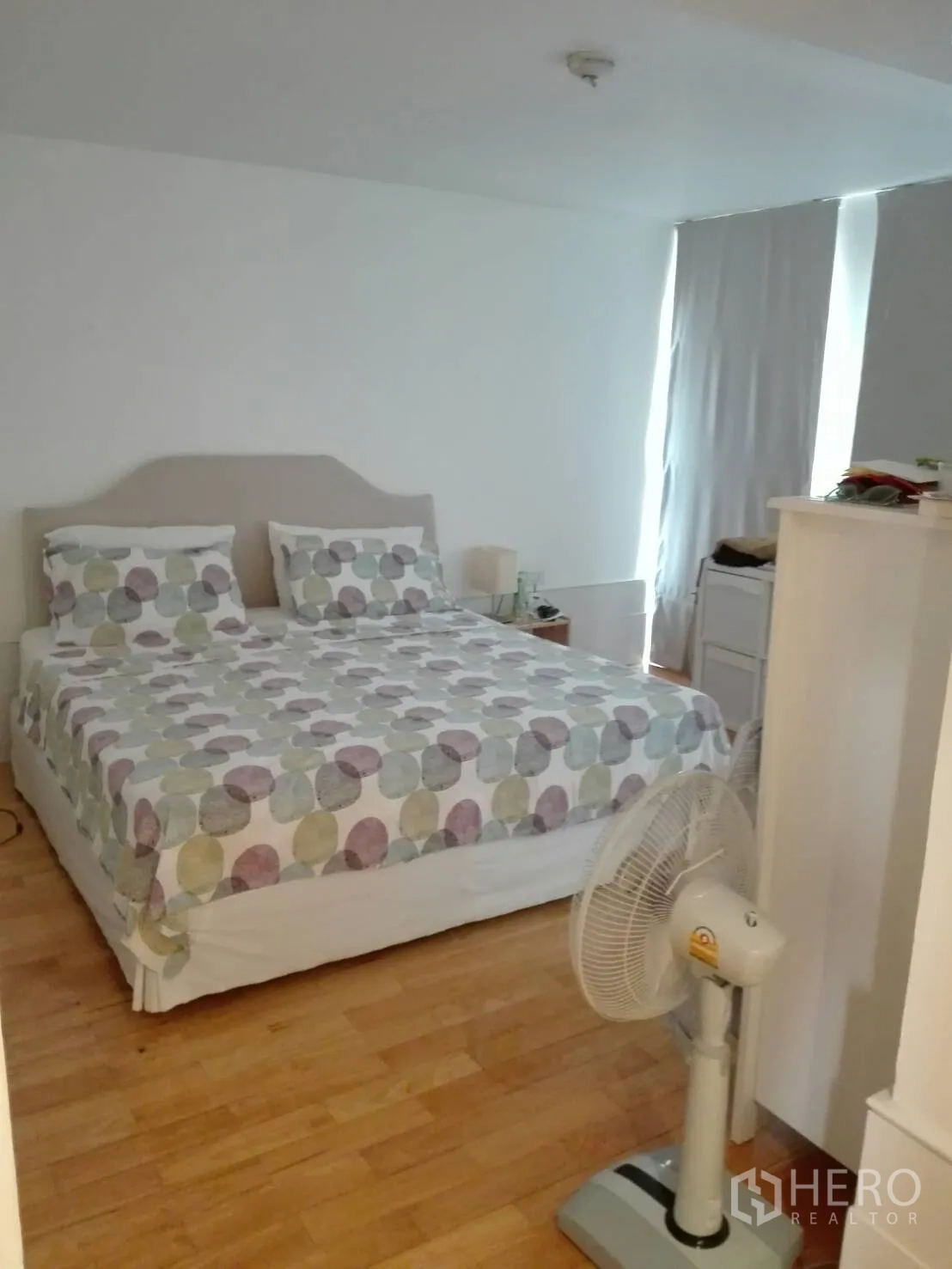 Condominium for rent in Khlong Toei, Bangkok - Spacious bedroom with double bed, light wood floors, tall curtains and a standing fan.