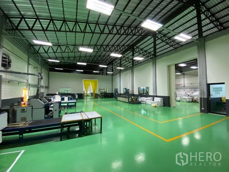 Factory for rent in Phra Pradaeng, Samut Prakan - High-ceiling production hall with green epoxy floor, steel truss roof, machinery, and LED lighting.