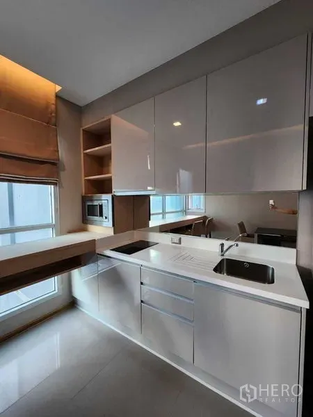 公寓 出售在Ratchathewi, Bangkok - 拉差贴威公寓厨房，亮面橱柜、灶台与水槽，临窗设有吧台。