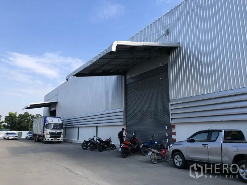 货栈 出租在Pathum Thani - Bang Khu Wat现代金属外墙仓库外观，宽幅卷闸门与带雨棚装卸区，卡车通行便捷