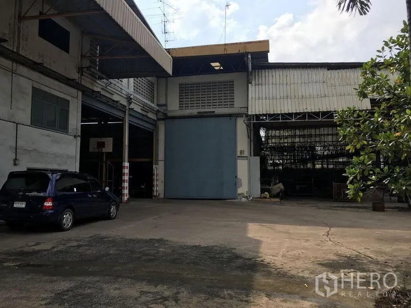 คลังสินค้า ให้เช่าในPhra Pradaeng, Samut Prakan - ด้านหน้าโกดังอุตสาหกรรม พระประแดง ประตูบานใหญ่สีน้ำเงิน ช่องโหลดสินค้ามีหลังคา และลานคอนกรีตกว้าง