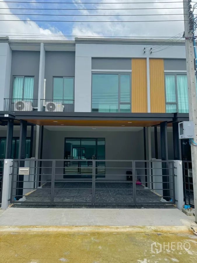 Townhouse for rent in Bang Phli, Samut Prakan - Modern two-storey townhome exterior with gated, covered parking for two cars.