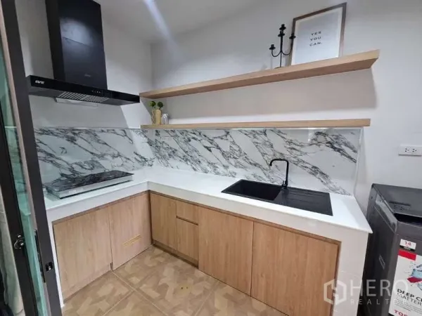 Townhouse for rent in Suan Luang, Bangkok - Compact kitchen with marble backsplash, black sink, cooktop, range hood and wood cabinets.