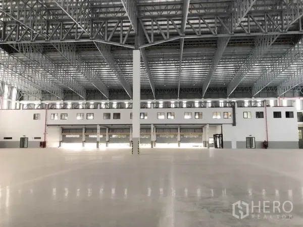 Factory for rent or sale in Samut Prakan - Central view of the warehouse showing several roller shutters and a tall column under the wide-span roof.