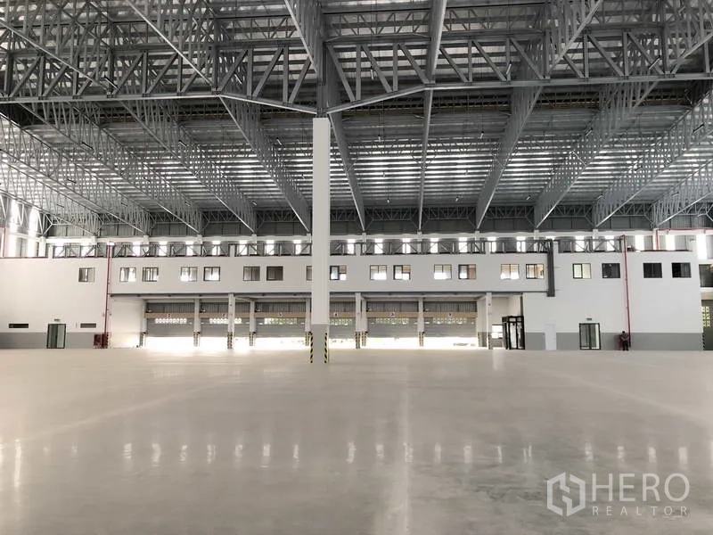 Factory for rent or sale in Samut Prakan - Central view of the warehouse showing several roller shutters and a tall column under the wide-span roof.