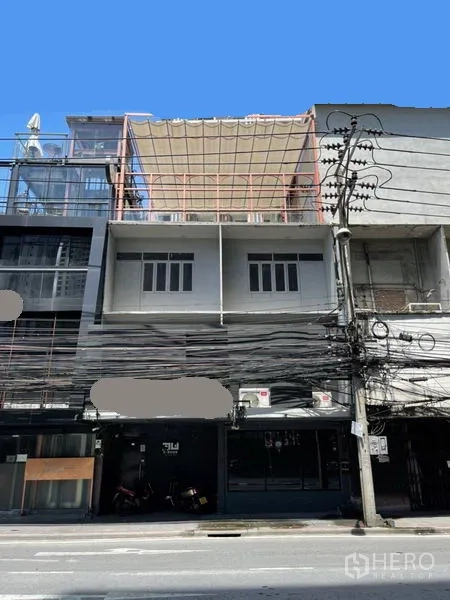 Shophouse for rent or sale in Watthana, Bangkok - Street-facing multi-storey shophouse facade with balcony and overhead utility lines.