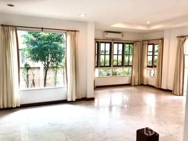 Detached House for rent in Saphan Sung, Bangkok - Large living room with multiple windows, cream curtains and garden views.