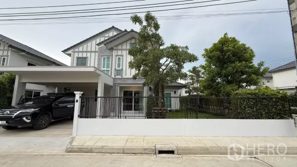 บ้าน ให้เช่าในBang Phli, Samut Prakan - บ้านเดี่ยวสองชั้นสไตล์โมเดิร์น มีที่จอดรถในร่มและสนามหญ้าหน้าบ้านหลังรั้วเหล็ก.