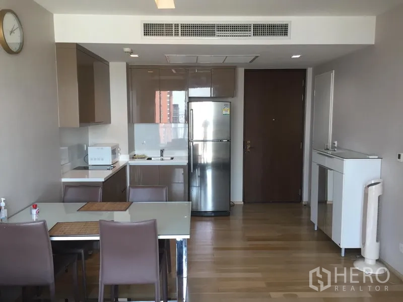 Condominium for rent in Khlong Toei, Bangkok - Open-plan kitchen and dining with glossy cabinetry, stainless refrigerator, and wood floors in a modern Sukhumvit condo.