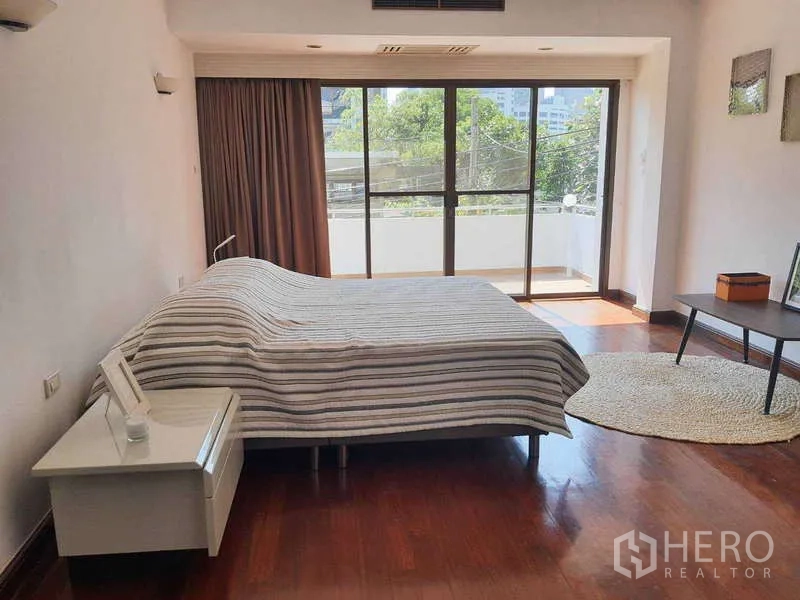 Townhouse for rent in Khlong Toei, Bangkok - Master bedroom with balcony access and views of greenery and city.